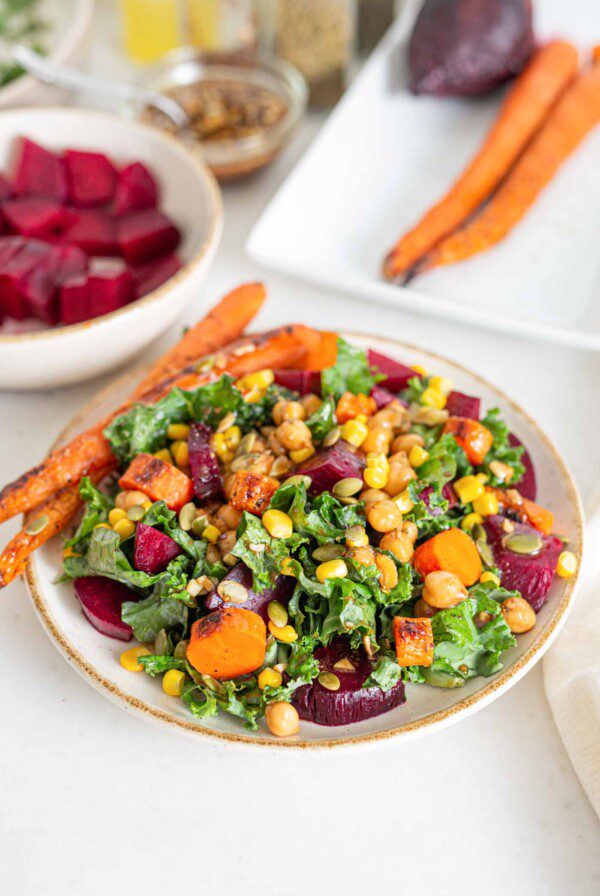 Bowl of kale salad with beet, corn, carrots and pumpkin seeds.