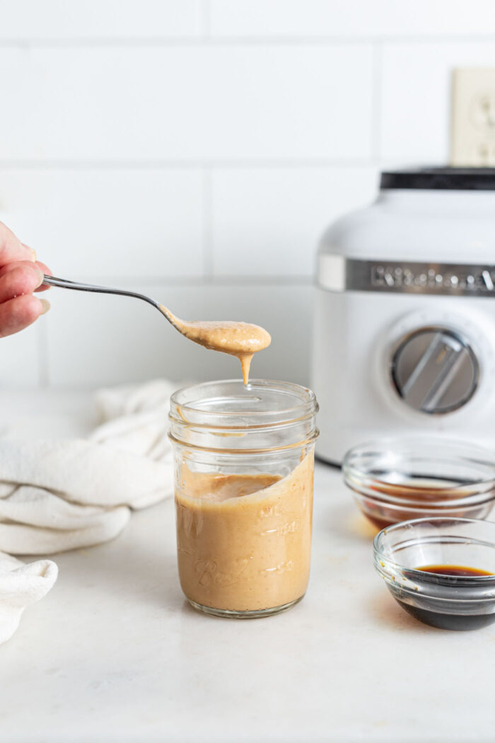 Scooping a spoonful of sauce out of a small jar.