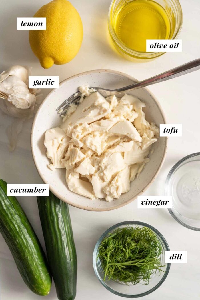Lemon, garlic, cucumber, oil, dill and tofu in containers.