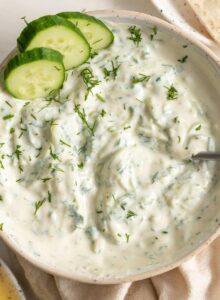 A bowl of tzatziki dip with a spoon in it.