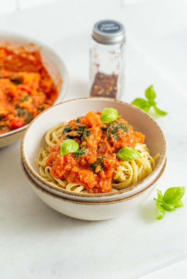 Bowl of pasta noodles with tomato vegetable sauce and fresh basil on top.