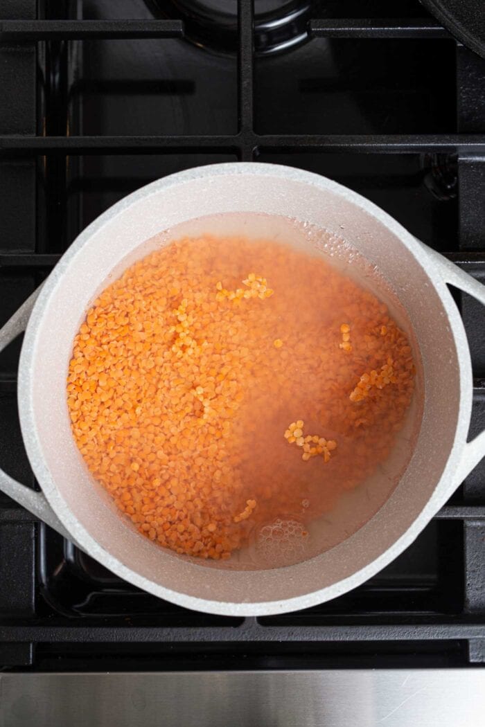 Red lentils cooking in a large pot on a gas range stovetop.