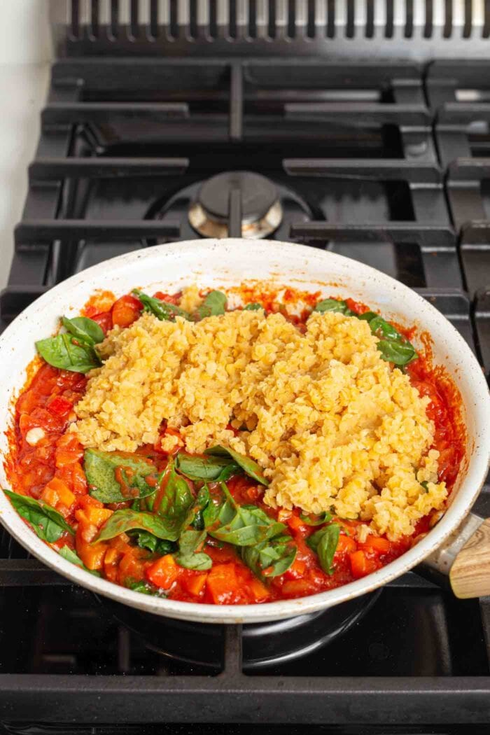 Red lentils and fresh spinach in a skillet of tomato sauce on a gas stovetop.
