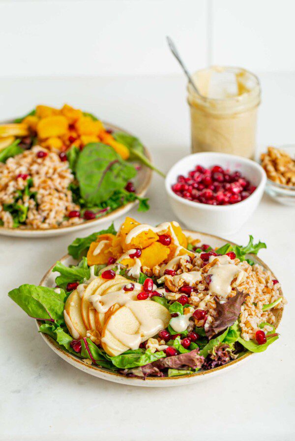 Two bowls of salad with apple, pomegranate, tahini sauce and walnuts.