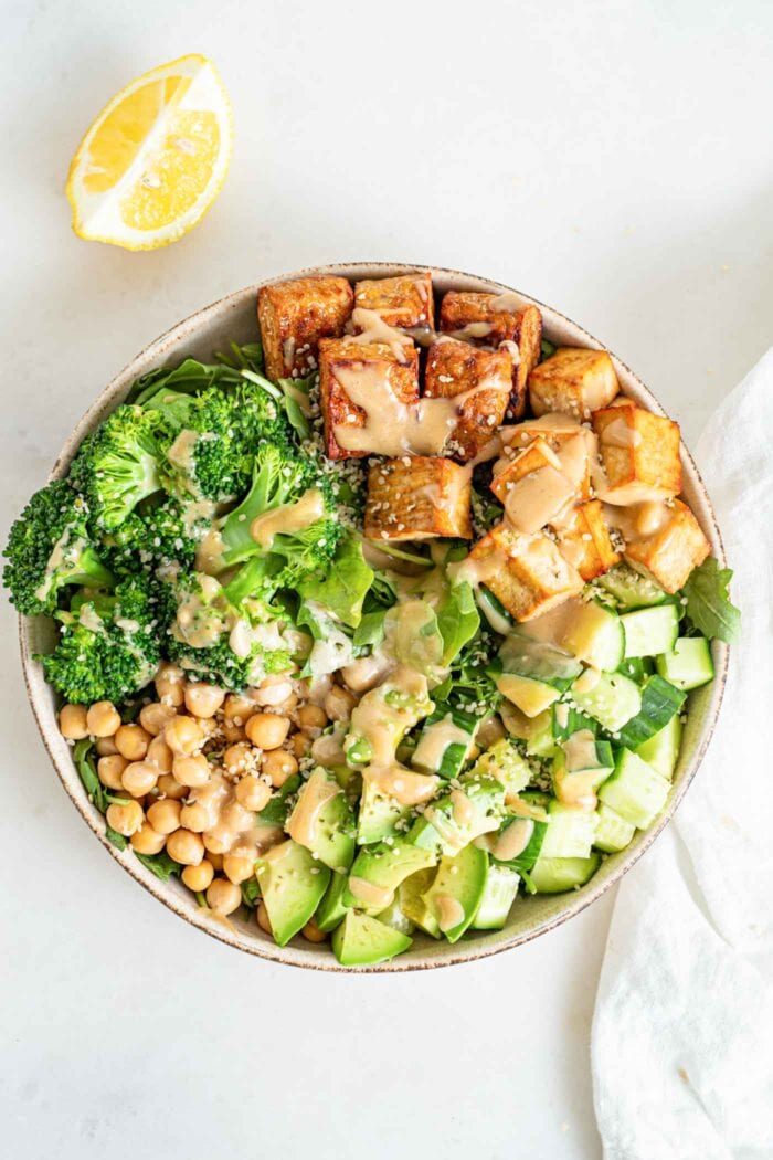 Overhead view of a green protein salad with tofu, tempeh, chickpeas, cucumber, broccoli and tahini.