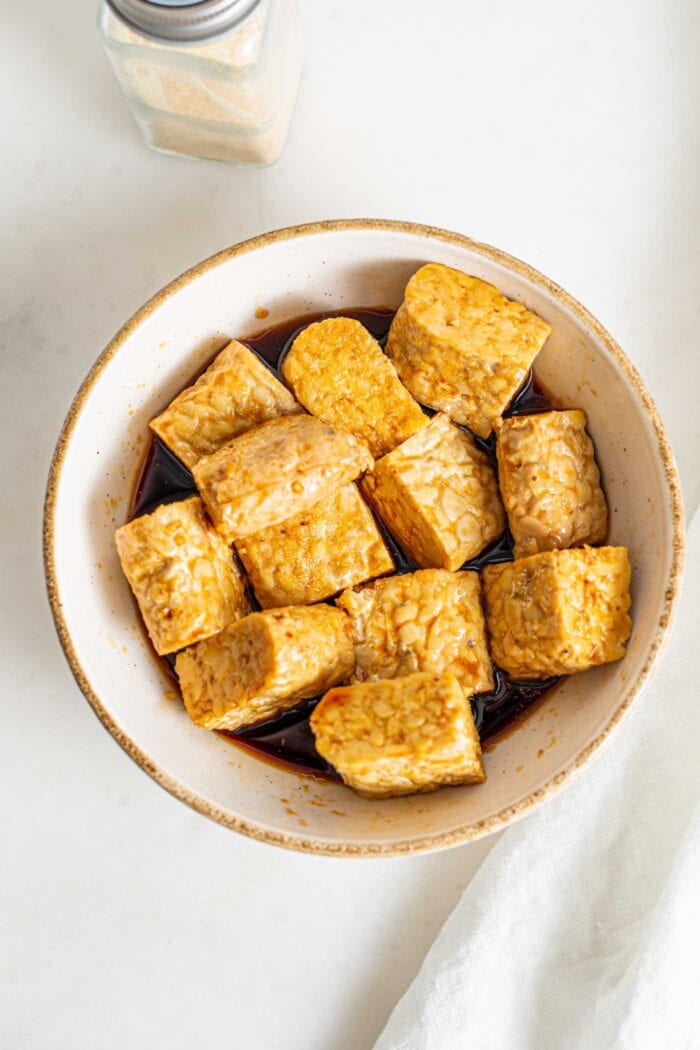 Cubed tempeh mixed in a small bowl with marinade.