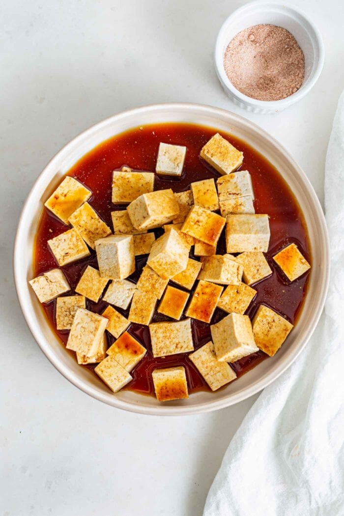 Cubed tofu mixed in a bowl with a soy sauce marinade.