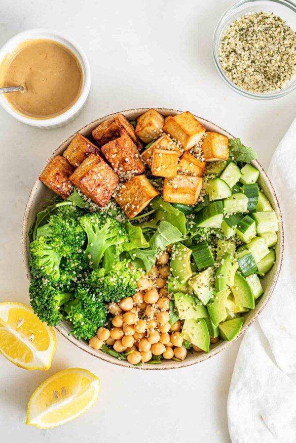 Overhead image of bowl of salad with broccoli, cucumber, chickpeas, tofu and tempeh.