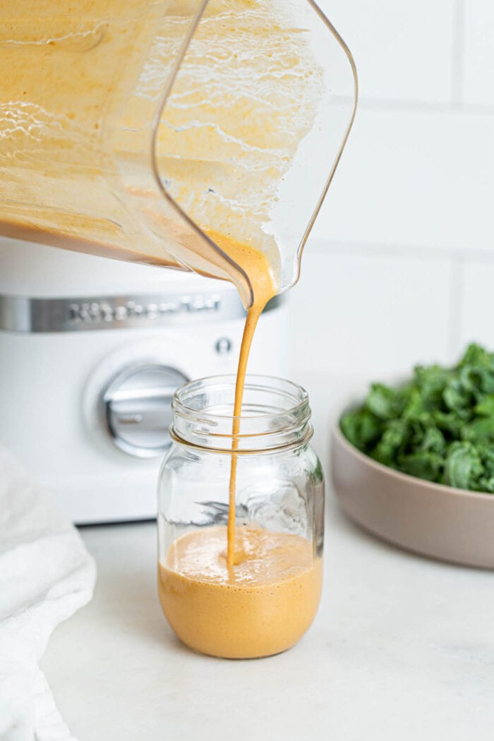 Pouring peanut sauce from a blender into a glass jar.