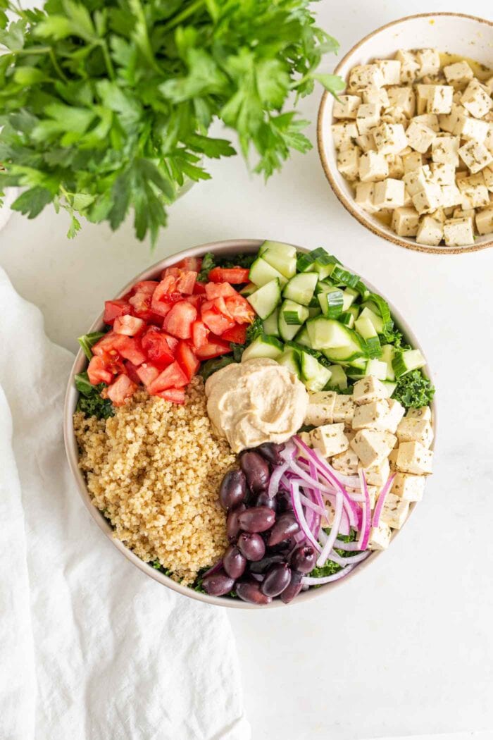 Overhead image of a bowl with quinoa, olives, chopped veggies and hummus.
