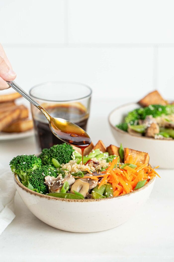 Adding a spoonful of teriyaki sauce to a bowl of stir fried vegetables.