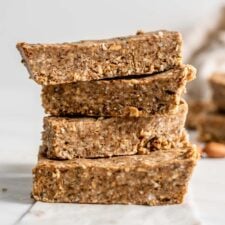 A stack of 4 energy bars with a few almonds scattered around them.