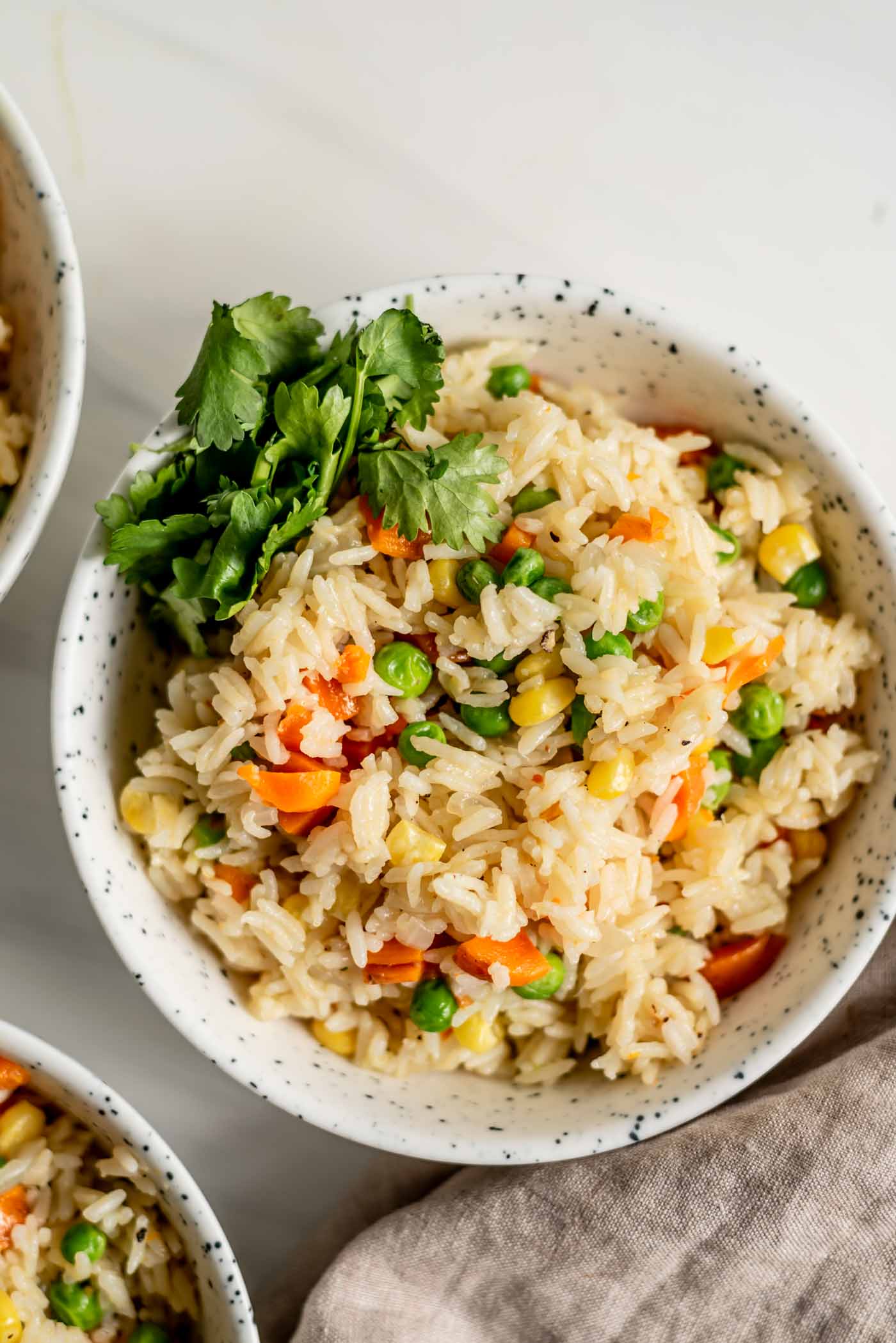 A bowl of rice pilaf with peas, corn and carrots and some cilantro on the side.