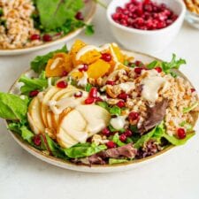 Two bowls of salad with apple, pomegranate, tahini sauce and walnuts.