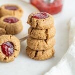 A stack of 4 thumbprint cookies beside a plate of cookies.
