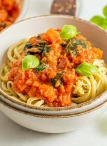 Bowl of pasta noodles with tomato vegetable sauce and fresh basil on top.