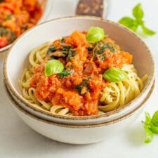 Bowl of pasta noodles with tomato vegetable sauce and fresh basil on top.