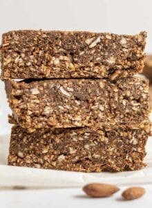 Stack of 3 energy bars on parchment paper with some almonds in the foreground.