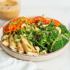 A bowl of tofu and fresh veggies on a counter with a jar of sauce in background.