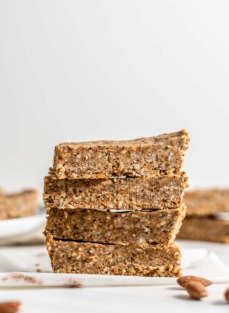 A stack of 4 energy bars with a few almonds scattered around them.
