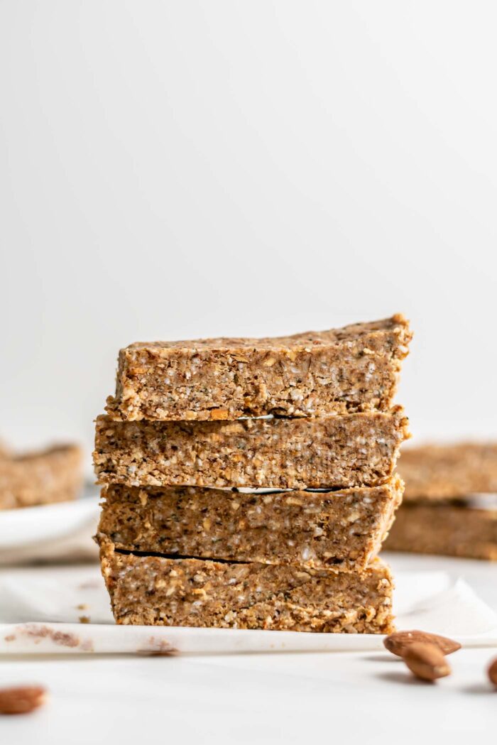 A stack of 4 energy bars with a few almonds scattered around them.