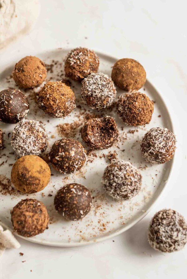 Plate of chocolate no-bake energy balls rolled in coconut, one has a bite out of it.