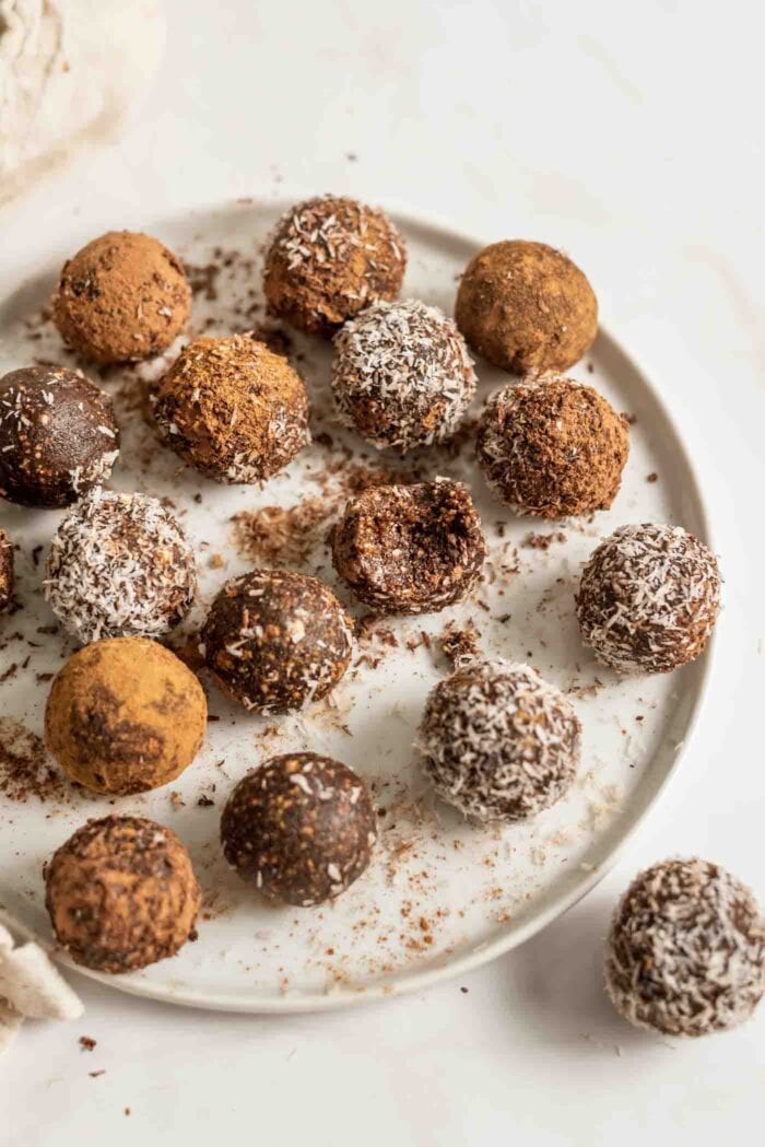 Plate of chocolate no-bake energy balls rolled in coconut, one has a bite out of it.