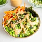 Carrot, edamame, rice, cucumber and nori topped with sauce in a bowl.