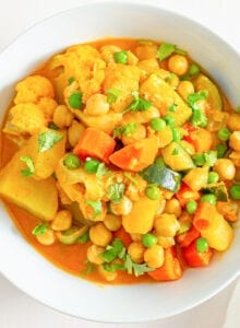 Overhead close up image of a bowl of stew with vegetables, chickpeas and peas.