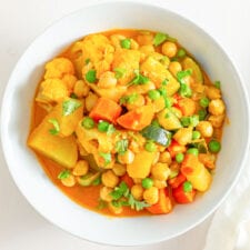 Overhead close up image of a bowl of stew with vegetables, chickpeas and peas.