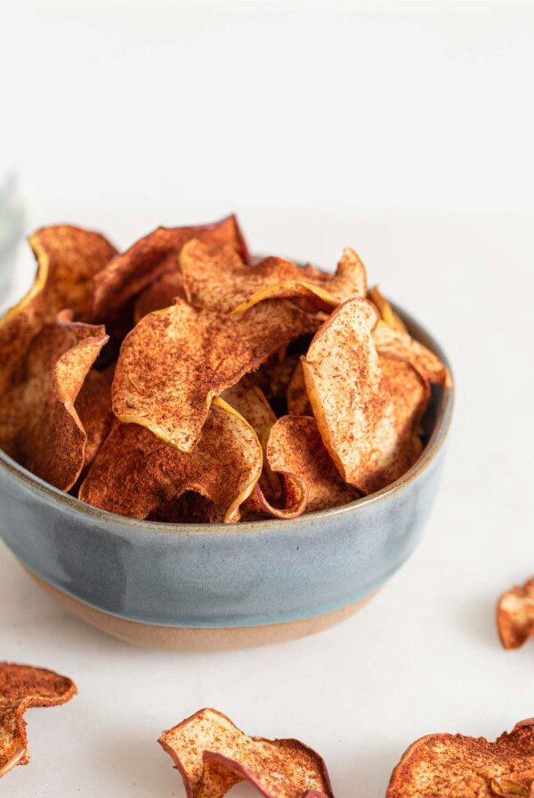 Bowl of baked apple chips, a few scattered around the bowl.