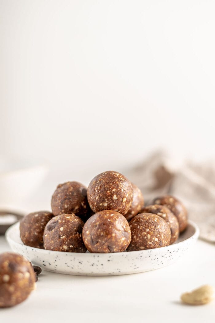 Plate of raw energy balls. Cashew and another ball rest in foreground.