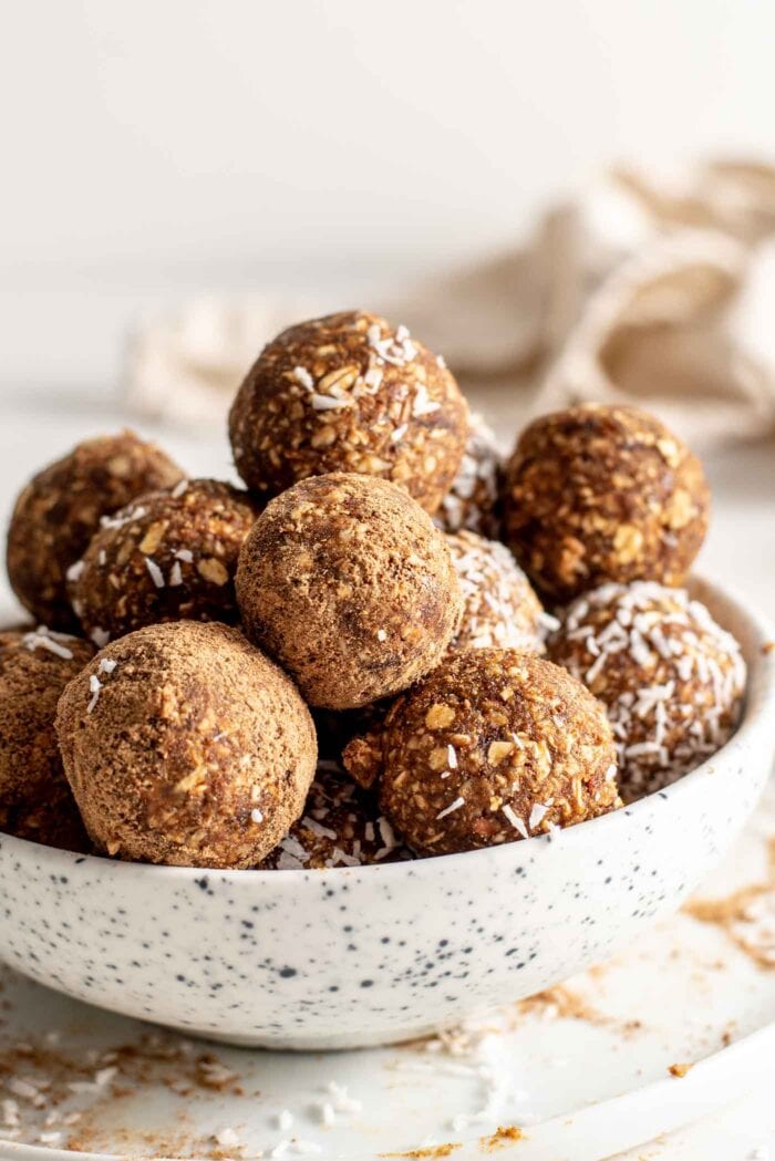Bowl full of energy balls. Some are coated in cinnamon or coconut.