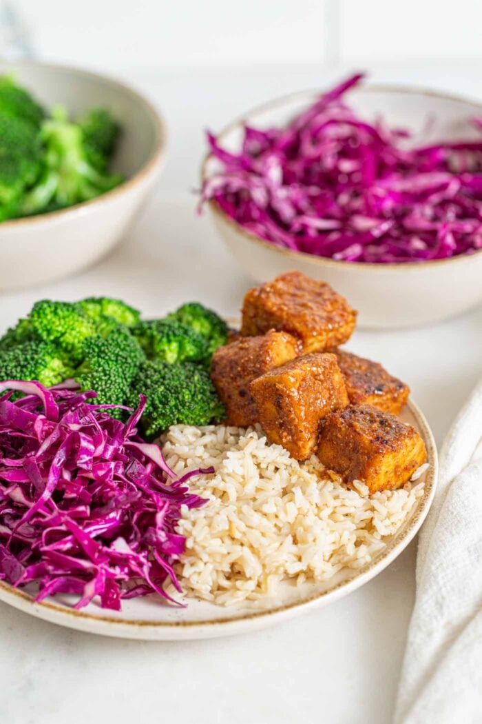 Bowl of brown rice, broccoli, sliced red cabbage and baked tempeh cubes.