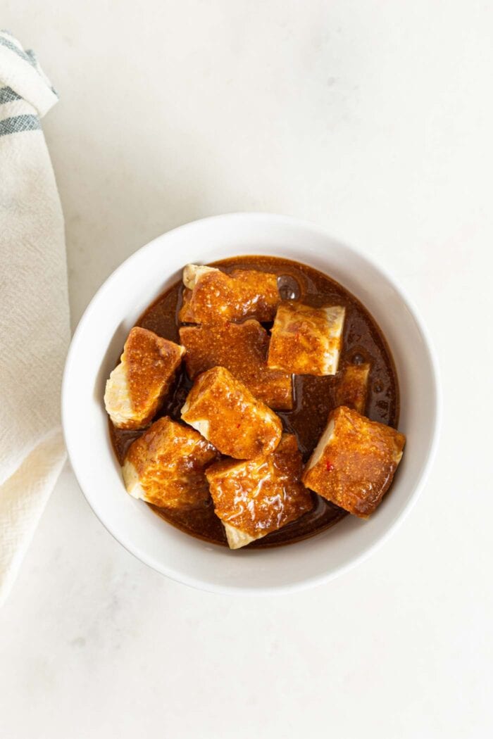 Cubes of tempeh marinating in a bowl of sauce.