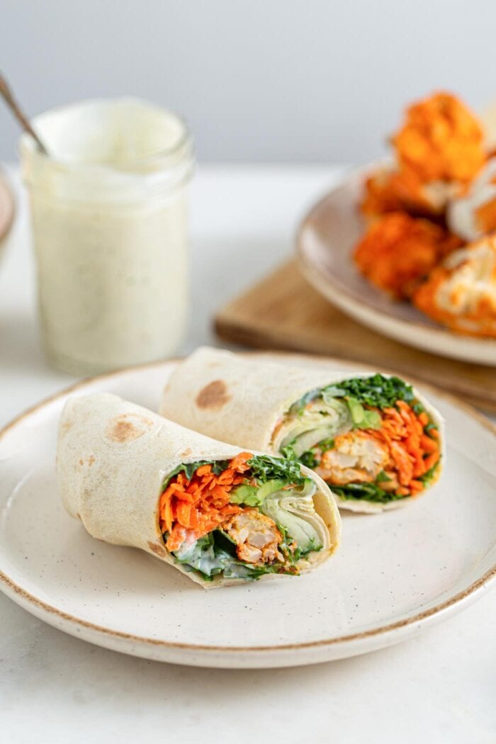Two halves of a buffalo cauliflower wrap with avocado on a plate, inside of wraps is showing.