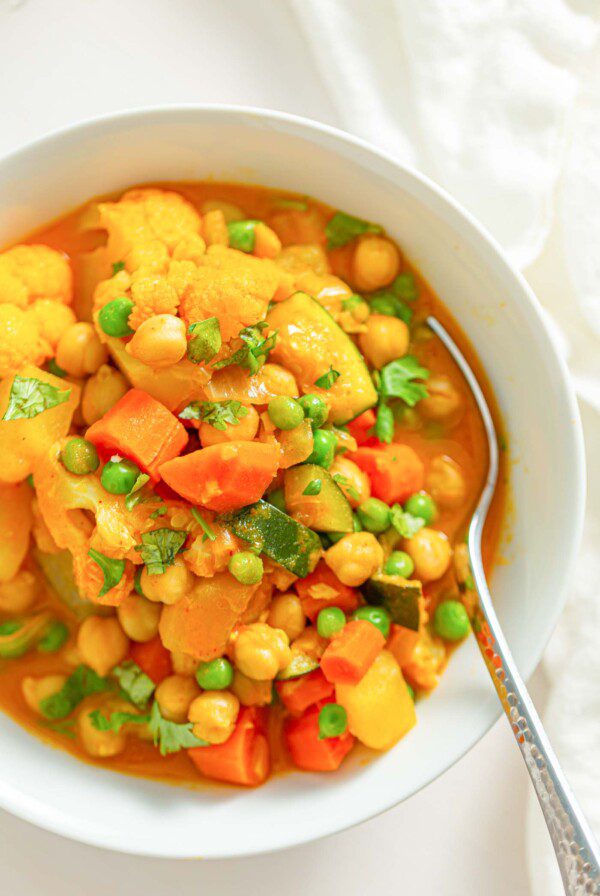 Overhead close up image of a bowl of stew with vegetables, chickpeas and peas.