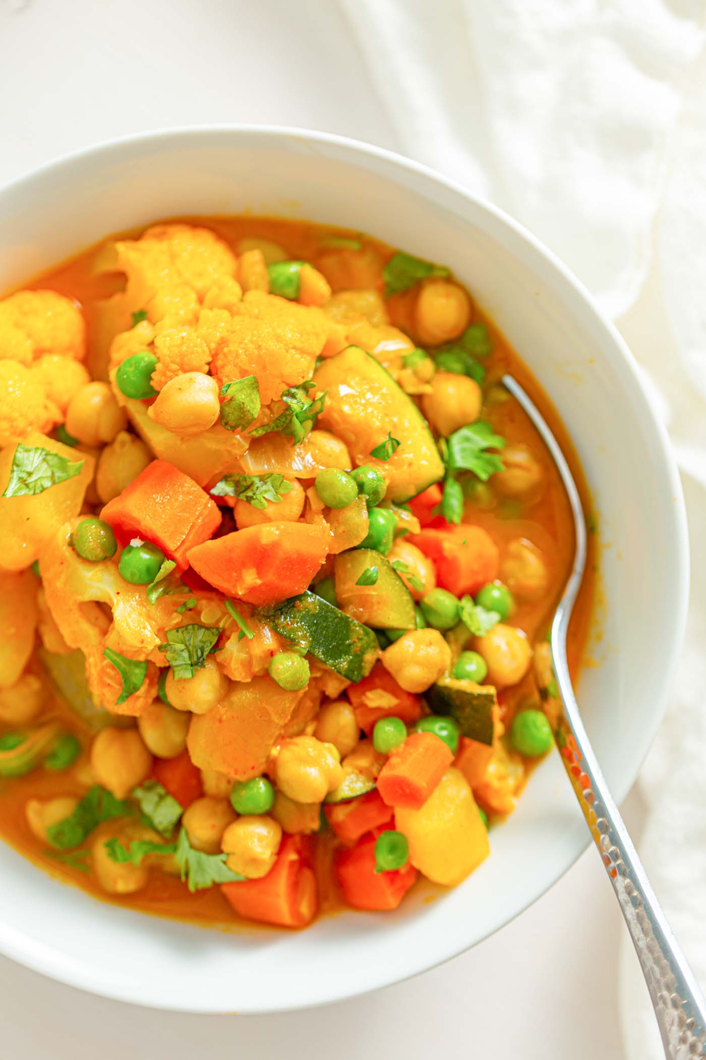 A bowl of stew with vegetables, chickpeas and peas and a spoon in it.