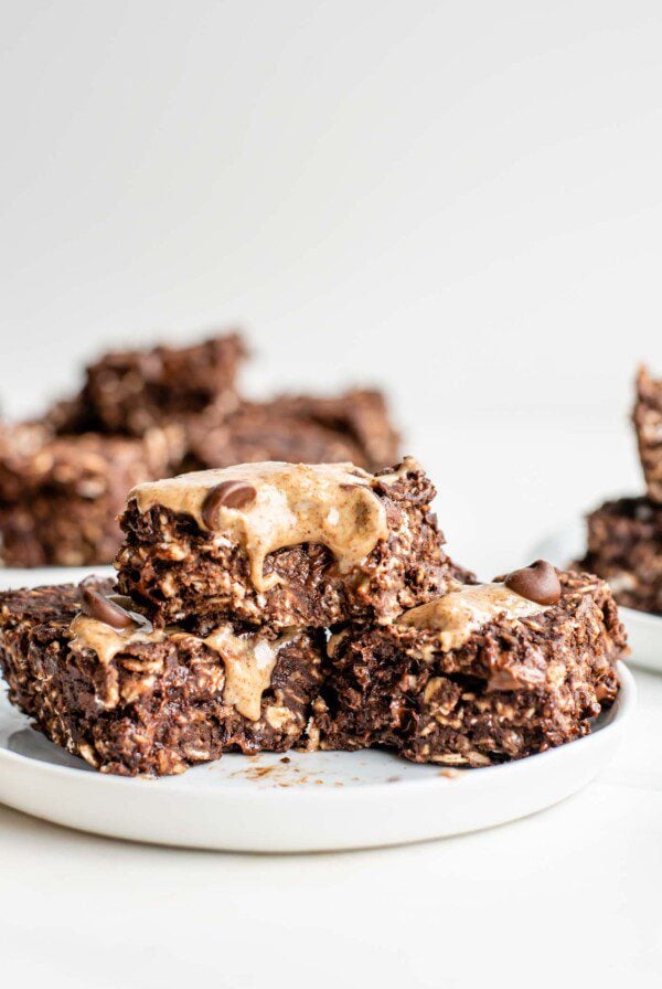 3 chocolate oatmeal bars with chocolate chips topped with almond butter on a plate.