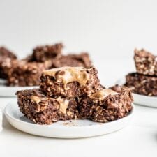 3 chocolate oatmeal bars with chocolate chips topped with almond butter on a plate.