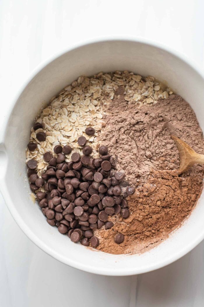 Protein powder, cocoa powder, chocolate chips and oats in a mixing bowl.