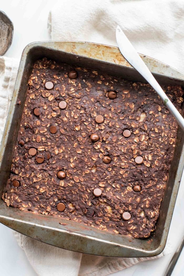 Baked chocolate oat bars in a baking pan. Knife rests on edge of pan.