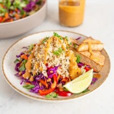 Bowl of colorful salad with brown rice, peanut sauce, tofu and veggies. Jar of sauce in background.