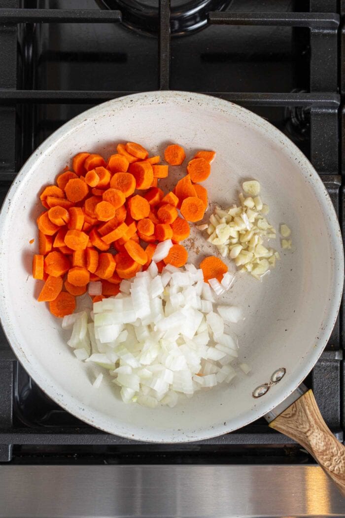 Diced onions, garlic and carrot cooking in a skillet on a stovetop.