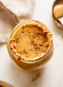 Overhead shot of a pumpkin smoothie in a jar. Spoon of peanut butter rests beside it.