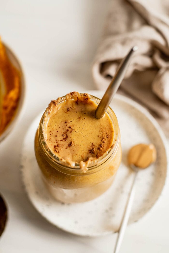 Overhead shot of a pumpkin smoothie in a jar. Spoon of peanut butter rests beside it.