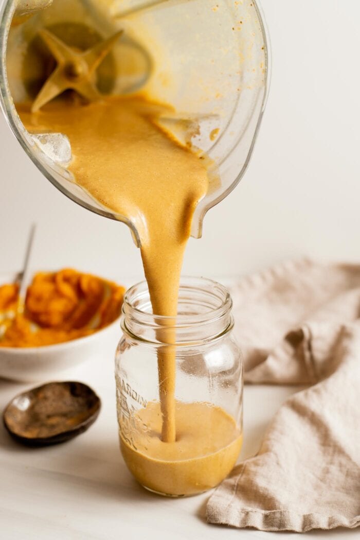 Blender pouring a pumpkin smoothie into a glass jar.