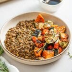 Lentils and roasted vegetables in a bowl. Small dish of balsamic dressing in background.