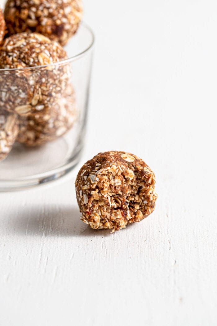 Close up of a cinnamon energy ball on a white surface with a jar of more energy balls in the background.