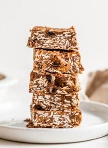 Stack of 5 chocolate oat bars on a plate. More bars in background.